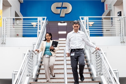 Medarbejdere hos Colgate-Palmolive går ned ad en trappe med et Colgate-Palmolive-logo bag sig på en blå væg.